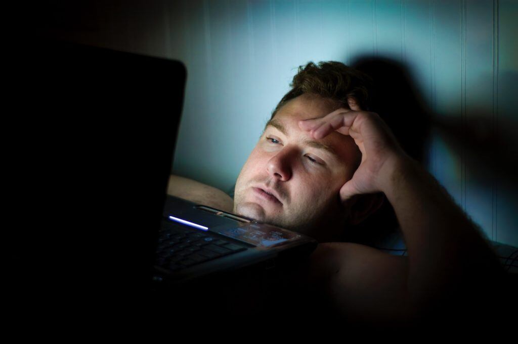 man in bed no sleeping looking at screen